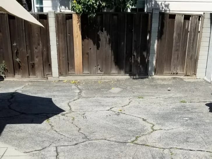 Cracked asphalt beside a wood fence before T&N Remodeling replaced it with pavers, Los Angeles